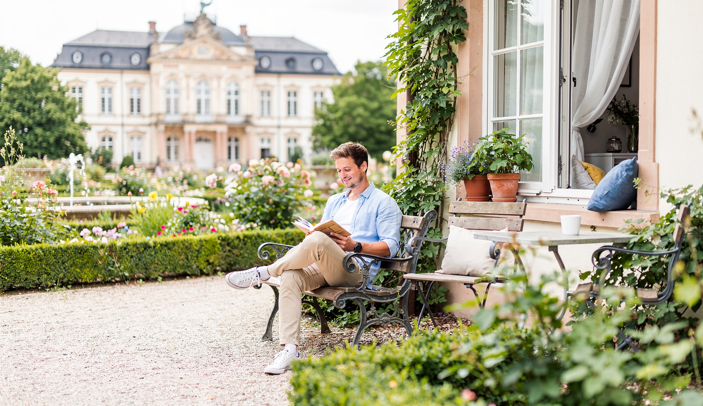 Student liest auf einer Bank in einem Schlossgarten.