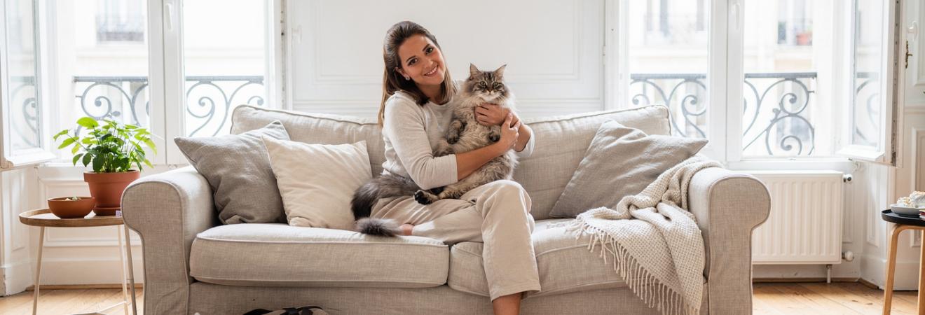 Frau kuschelt mit einer Katze auf einem Leinensofa.