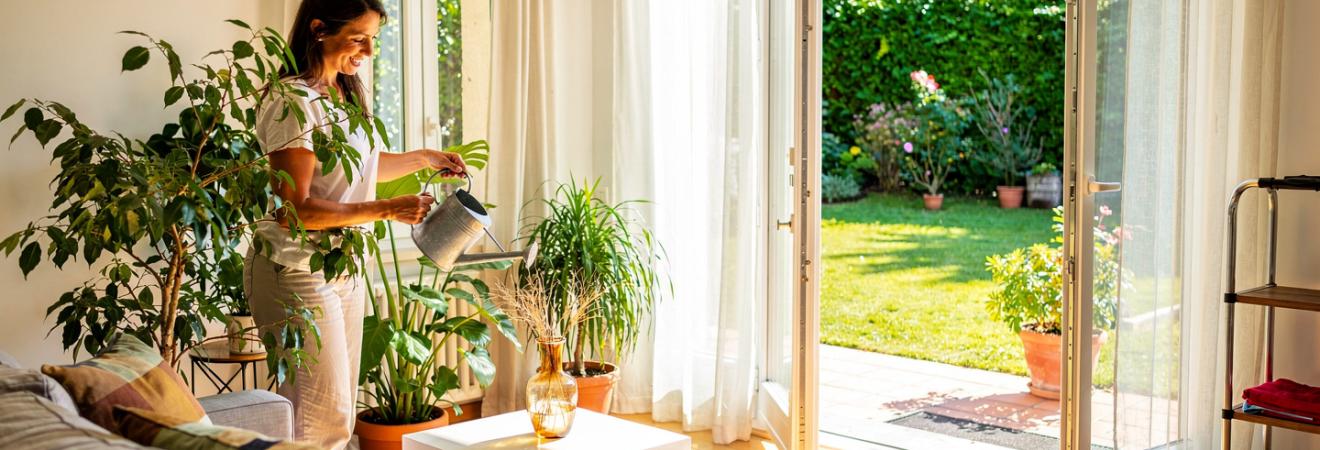 Frau gießt Pflanzen in einem sonnigen Ferienhaus.