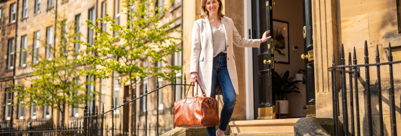 Frau mit Reisetasche vor einem Sandsteinhaus in Edinburgh.