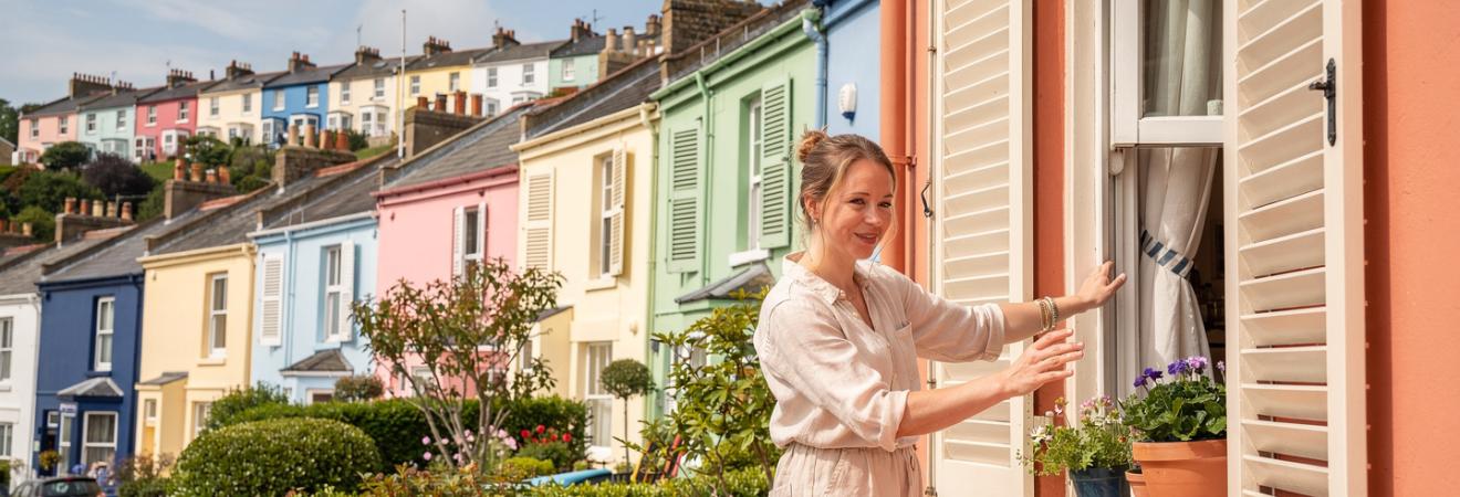 Frau öffnet die Fensterläden eines bunten Hauses in Bristol.