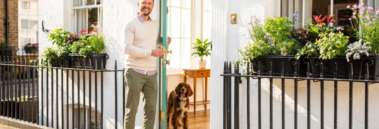 Mann schließt eine Londoner Mews-Haustür auf, Hund im Flur.