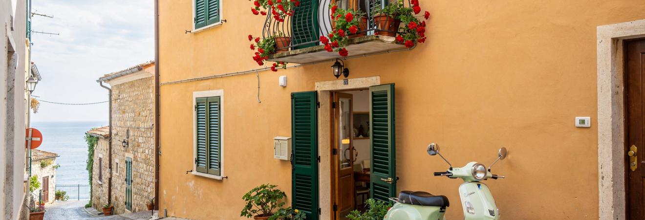 Ockerfarbenes Stadthaus in einer italienischen Gasse mit Geranienbalkon.