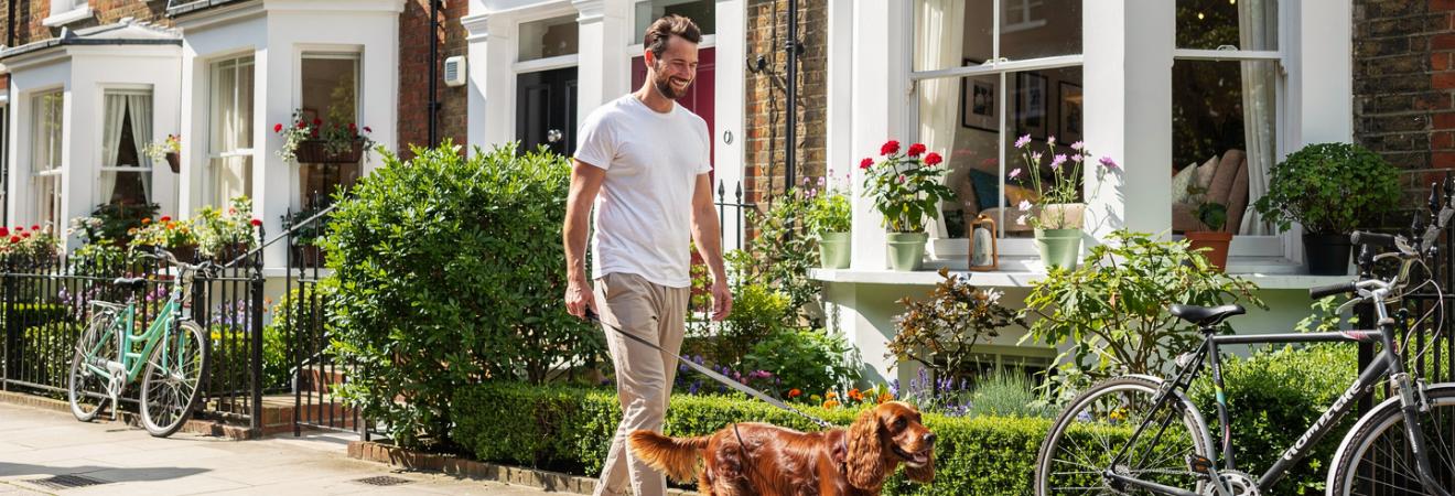 Mann geht mit einem Spaniel durch eine Londoner Wohnstraße.